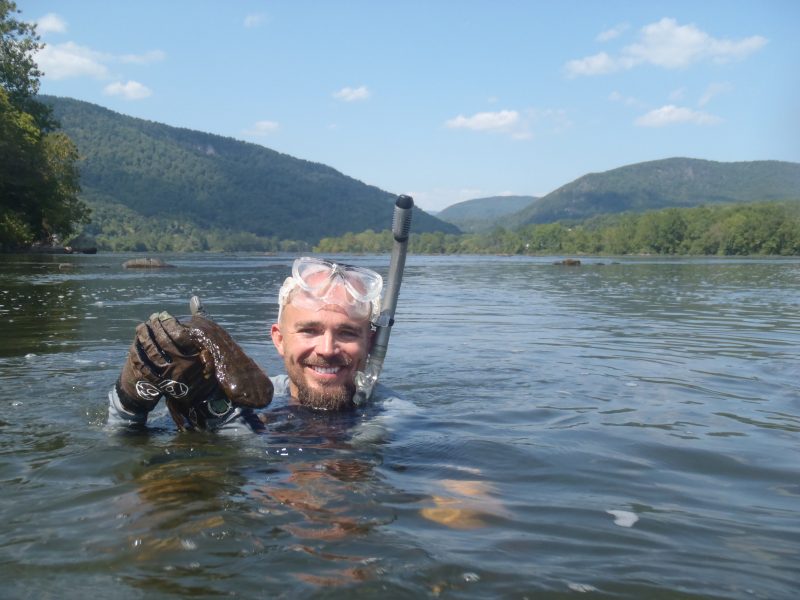 Bill Hopkins holding a Hellbender in the water, with the Appalachian mountains on the horizon